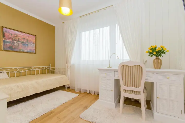Dormitorio con paredes doradas, cama blanca y escritorio. Los colores que combinan con el amarillo en paredes son el blanco y los tonos tierra, creando un ambiente cálido y luminoso.