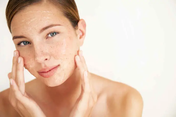 Mujer aplicándose una mascarilla exfoliante con vinagre de manzana para la cara. Sus dedos masajean suavemente el producto.