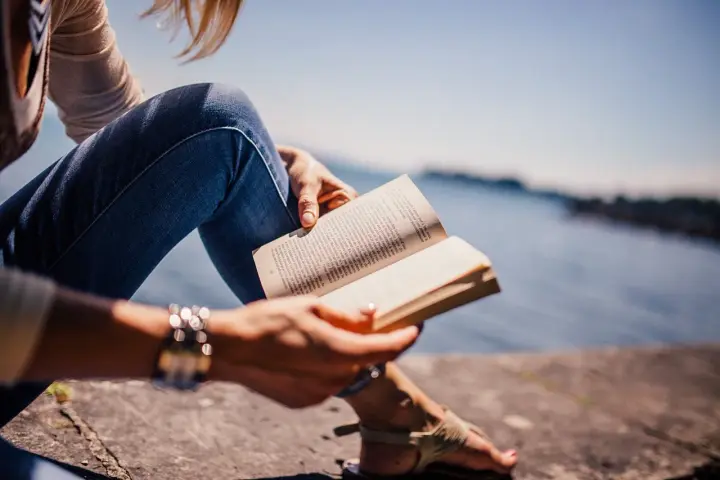 Persona sentada junto al agua, leyendo un libro en francés.