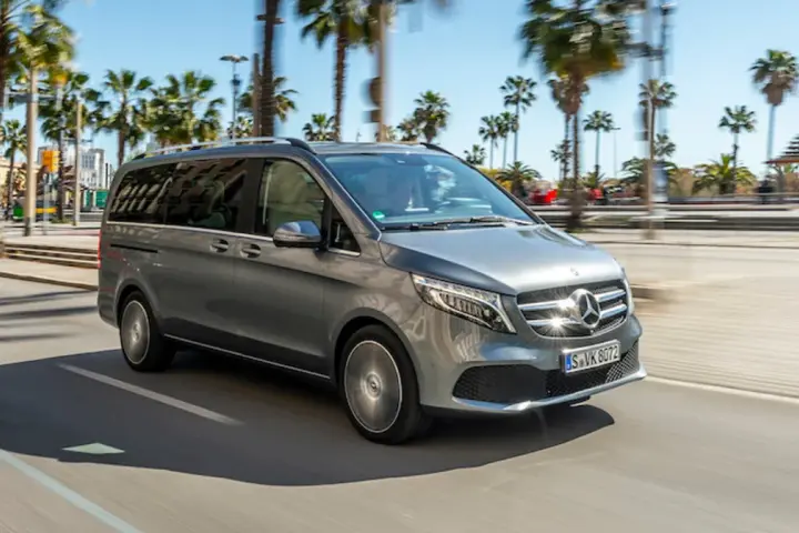 Szary Mercedes minivan jedzie ulicą w słoneczny dzień, otoczony palmami.