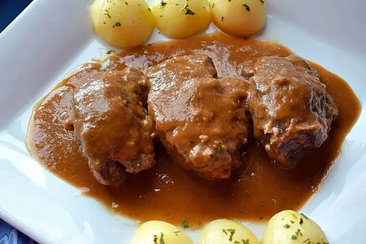 Tres tiernas carrilleras al vino tinto, bañadas en su salsa, acompañadas de patatas cocidas con perejil.