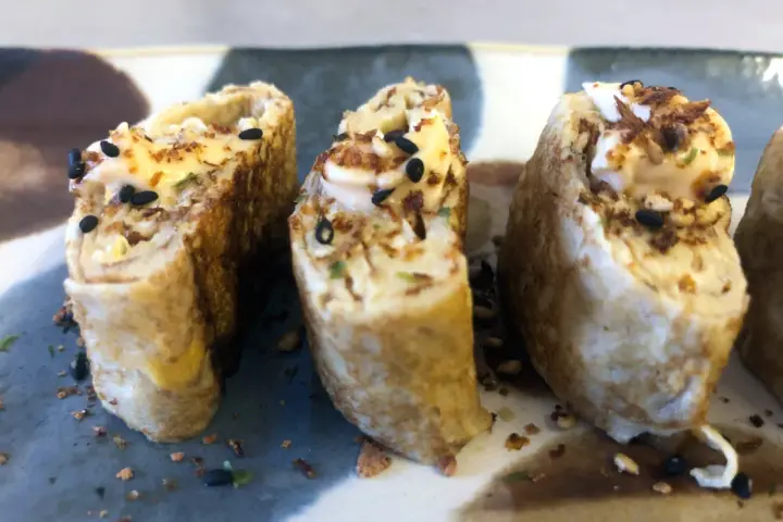 Trzy kawałki sushi w omlecie, polane majonezem i posypane czarnym sezamem.