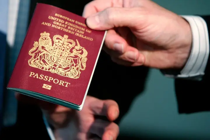 Dłoń podaje paszport biometryczny Wielkiej Brytanii. Widoczny herb i napis "PASSPORT".