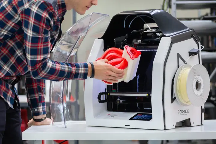 Inżynier wyjmuje z drukarki 3D skomplikowany element, pokazując potencjał druku 3D w przemyśle.