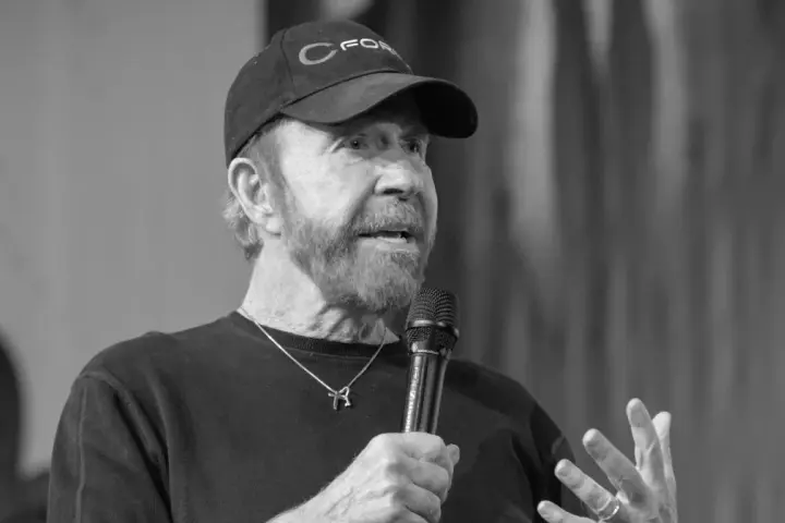 Chuck Norris, mimo swojego wieku, wciąż ma charyzmę. Mówi do mikrofonu w czapce z daszkiem.