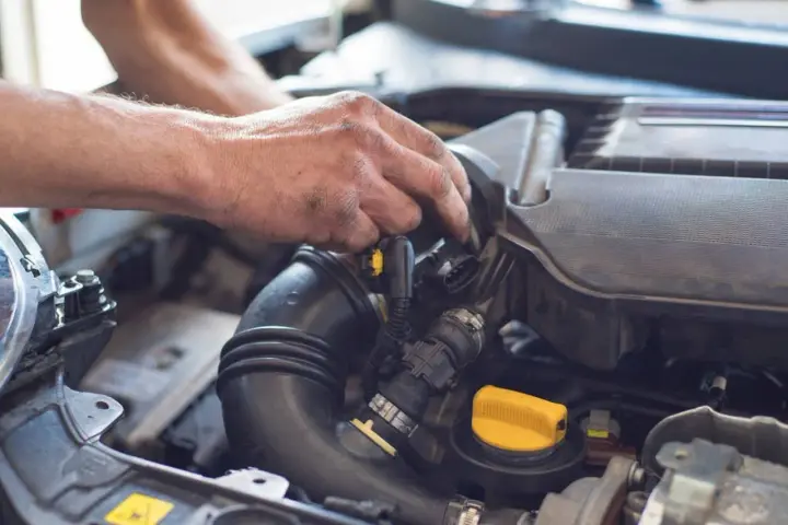 Ręce mechanika pracują przy silniku. Widoczny jest czarny przewód dolotowy i żółta zakrętka. p0101.