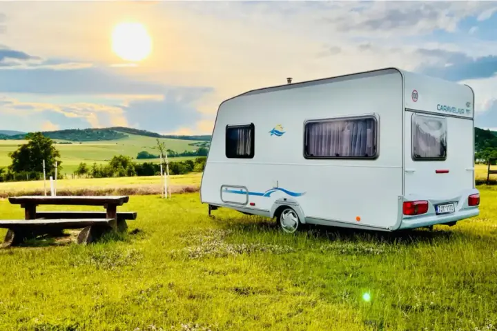 Przyczepa Caravelair zaparkowana na łące o zachodzie słońca. W tle malownicze wzgórza i pola.