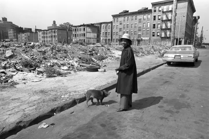 Une femme et son chien devant des immeubles délabrés et des décombres.