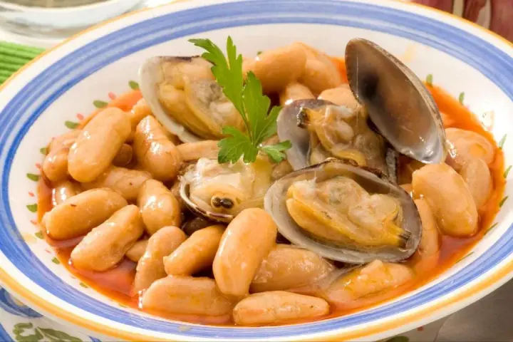 Plato de fabes con almejas, un guiso tradicional asturiano con judías blancas tiernas y jugosas almejas, decorado con perejil fresco.