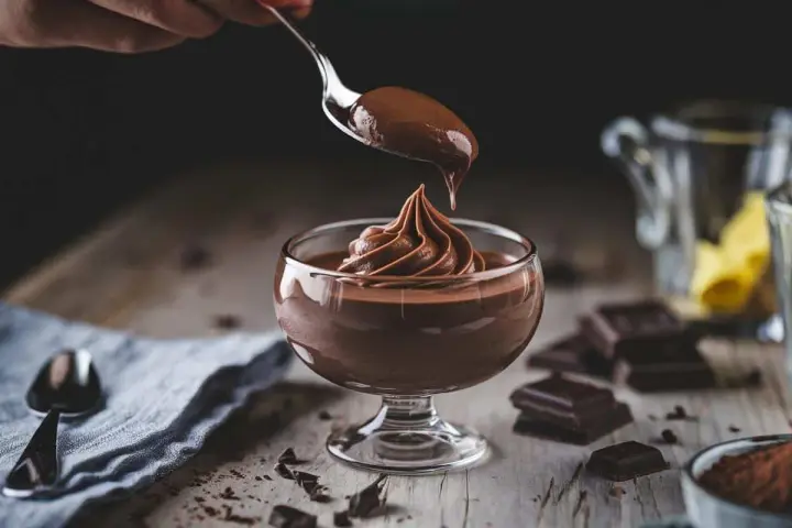 Ein Löffel mit cremigem Mousse au Chocolat tropft auf eine kunstvoll aufgespritze Portion in einem Glas.