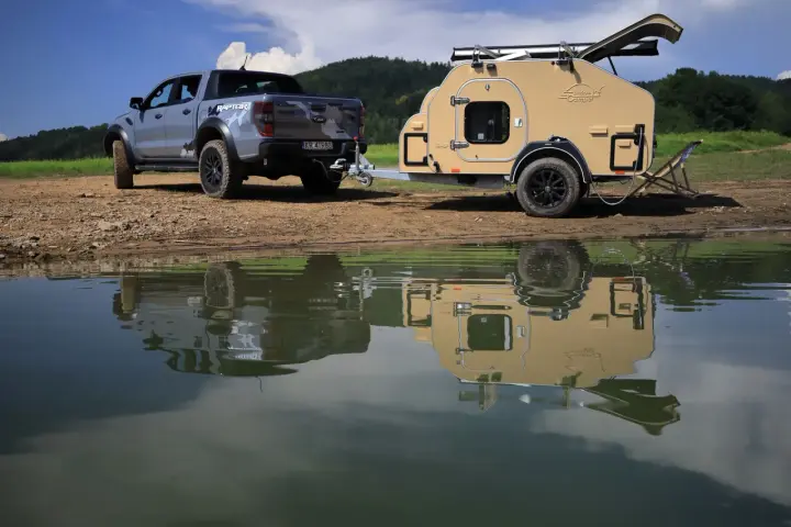 Srebrny Ford Raptor z przyczepą wyprawową Lifestyle Camper nad jeziorem.