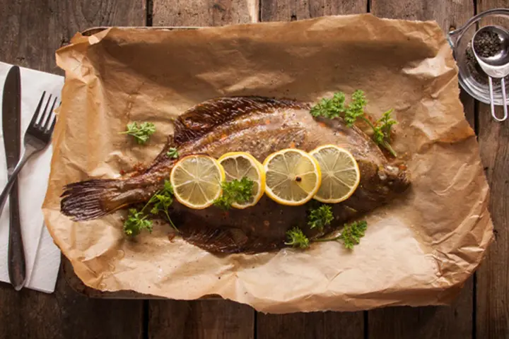 Gebackene Scholle mit Zitronenscheiben und Petersilie auf Backpapier. Perfekt zum Scholle essen!