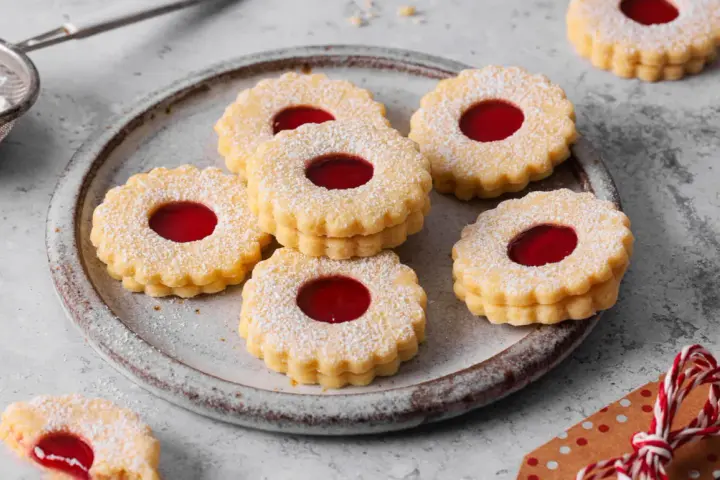 Ein Teller voller **die besten Spitzbuben der Welt**, bestäubt mit Puderzucker, mit leuchtend roter Marmeladenfüllung.