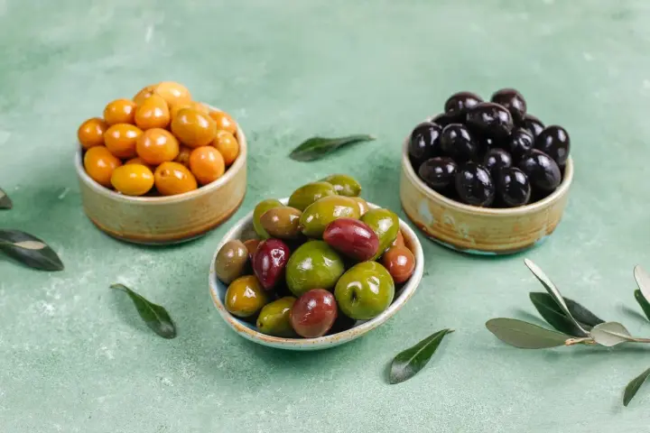 Tres cuencos con aceitunas de diferentes colores: amarillas, verdes y negras.