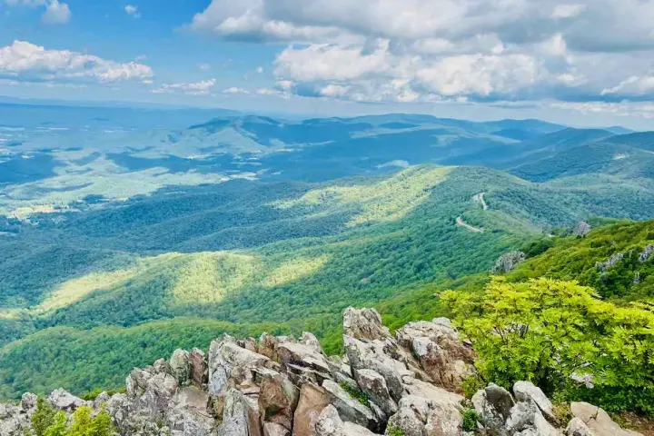 Scenic mountain vista, perfect for day trips from Richmond VA. A winding road snakes through lush green hills under a bright, cloudy sky.