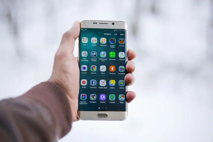 Dłoń trzymająca złoty telefon Samsung z ikonami aplikacji na ekranie.