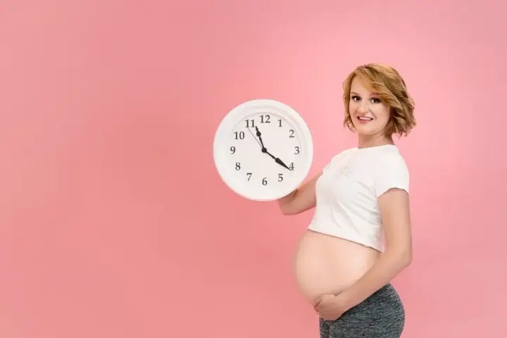 Czekasz na poród? Zegar w rękach ciężarnej sugeruje, jak przyspieszyć poród, choć to tylko symboliczne pytanie.