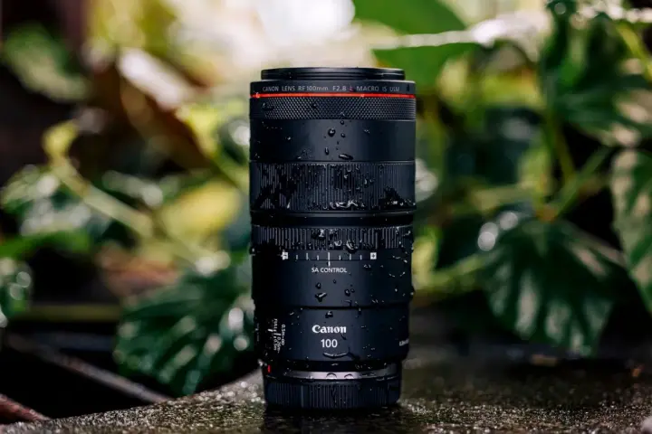 Objectif Canon RF 100mm f/2.8 Macro IS USM, couvert de gouttes d'eau, prêt pour un test en extérieur.