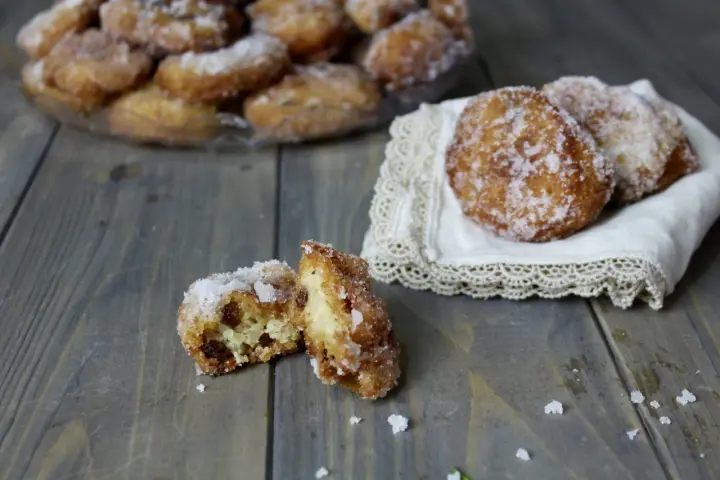Frittelle di riso ricetta della nonna: dolcetti dorati e zuccherati, uno aperto rivela l'interno soffice e i chicchi d'uva passa.