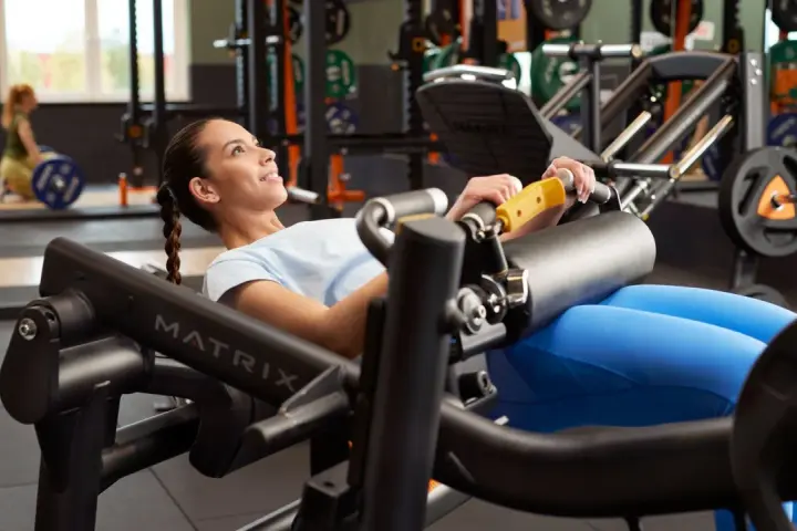 Femme souriante effectuant un hip thrust sur une machine de musculation, concentrée sur son entraînement.