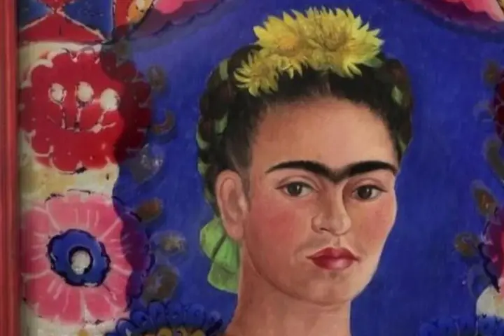 Portrait de Frida Kahlo, icône féministe, ornée de fleurs jaunes et d'un ruban vert, sur fond bleu vibrant et motifs floraux colorés.
