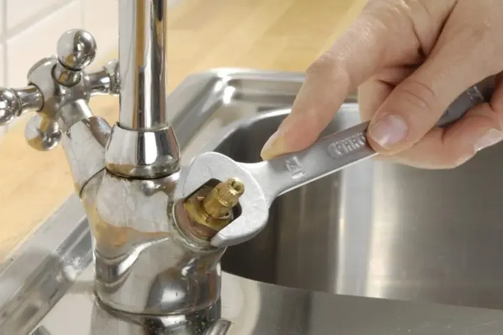 Hand repariert tropfenden wasserhahn mit einem Schraubenschlüssel.