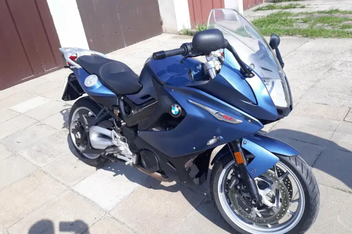 Błękitny motocykl BMW F800 GT stoi na chodniku przed garażem.