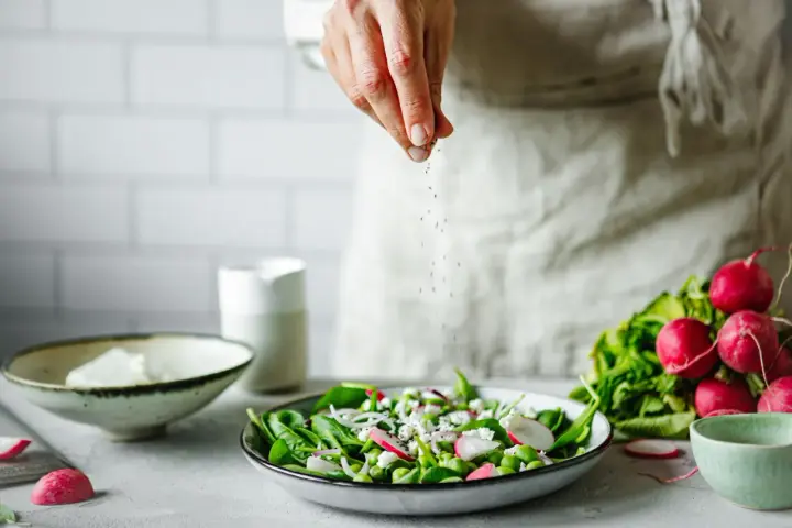 Une main saupoudre des graines sur une salade fraîche. Une idée pour une recette de radis noir.