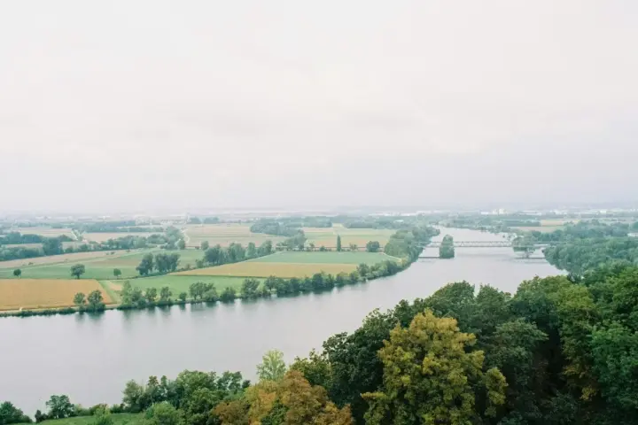 Szeroka rzeka na tle zielonych pól i lasów. W oddali widać most i zabudowania.