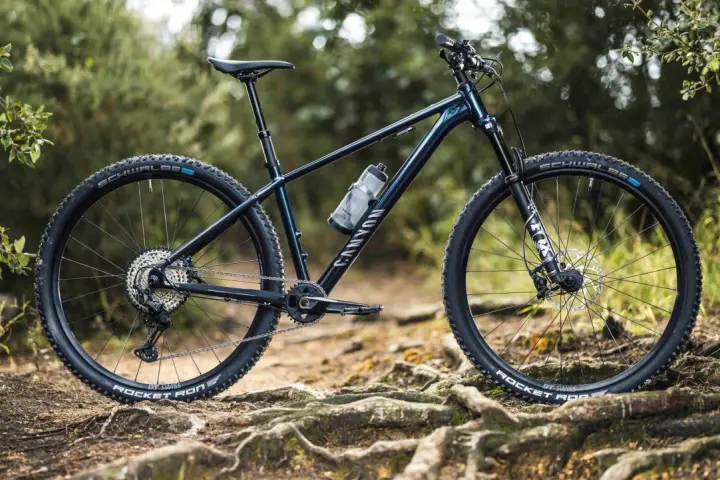 Muscle bike Canyon blu scuro su sentiero sterrato con radici affioranti.