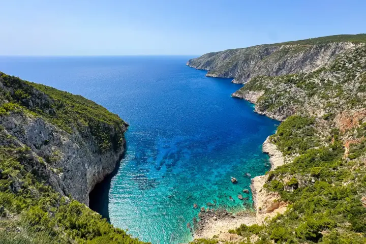 Widok na zatokę z klifami porośniętymi zielenią. Idealne miejsce na zakynthos wycieczki fakultatywne, by podziwiać turkusową wodę.