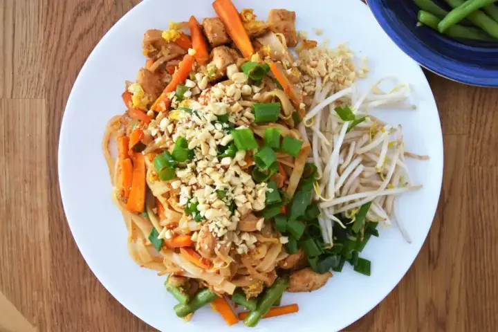 Pyszny sos pad thai z kurczakiem, warzywami i orzeszkami ziemnymi, podany z kiełkami fasoli mung.