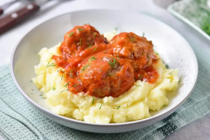 Pyszne pulpeciki w sosie pomidorowym na kremowym purée ziemniaczanym, posypane świeżym koperkiem.