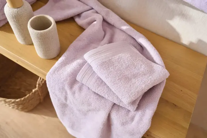 Variedad de tipos de toallas de baño en color lavanda, apiladas sobre una superficie de madera.