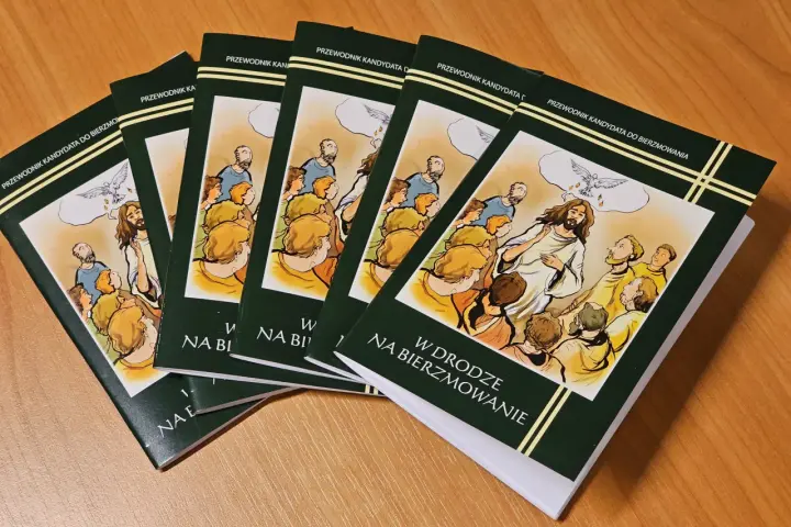 Kilka zielonych książek z ilustracją Jezusa i gołębicy na drewnianym stole.