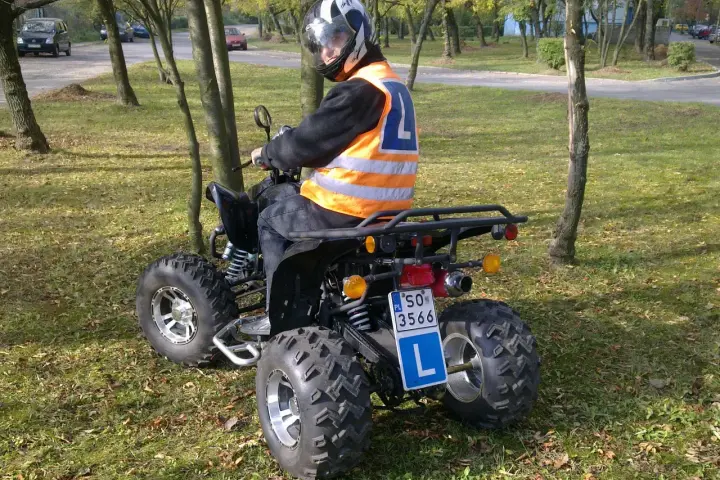 Młody kierowca w kamizelce odblaskowej i kasku uczy się jeździć quadem. Tablica z literą "L" wskazuje, że to kategoria B1.
