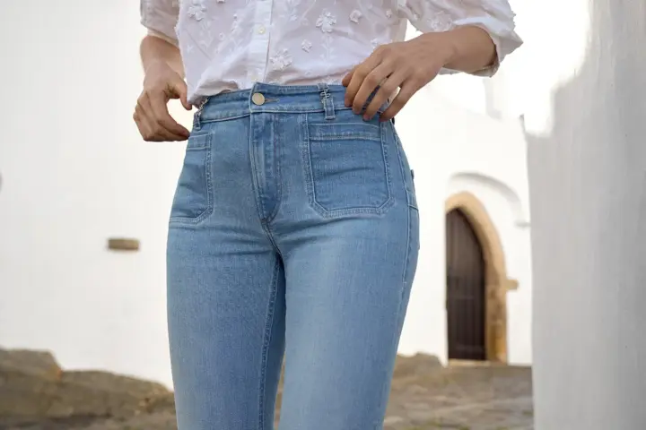 Mujer con vaqueros de tiro alto y camisa blanca, ajustándose la cintura.