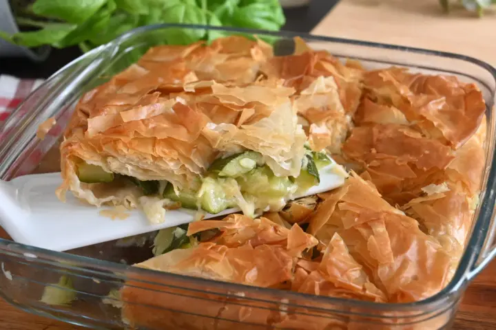 Una fetta di torta salata con zucchine, con croccante pasta sfoglia dorata e ripieno filante.