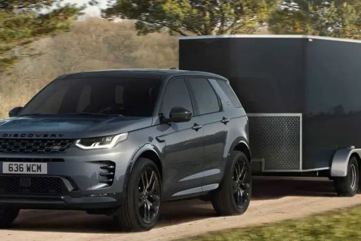 Szary Land Rover Discovery Sport z przyczepą o masie 2000 kg jedzie po leśnej drodze.