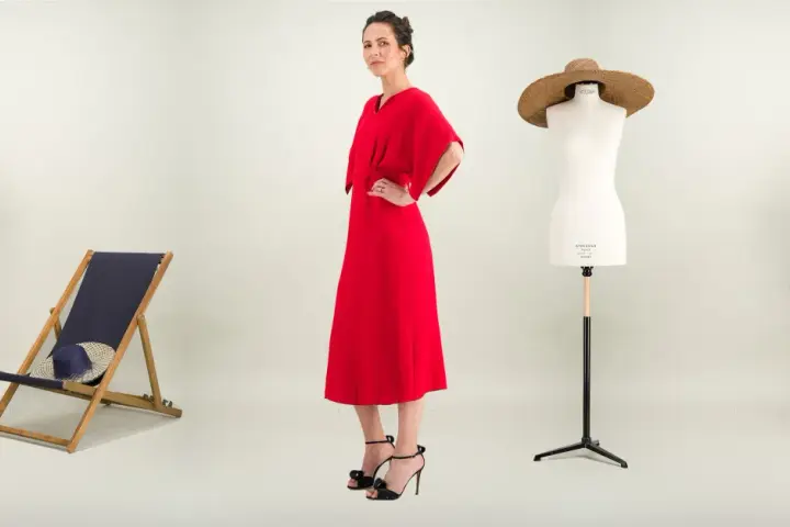 Une femme pose dans une robe rouge éclatante. À ses côtés, une chaise longue, un mannequin de couture et des plantes. Une robe casual, c'est quoi ?