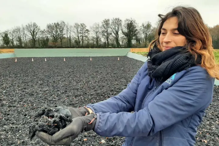 Une femme tient dans ses mains un échantillon de fibre, un avis carrière en fibre. L'arrière-plan montre une carrière équestre.
