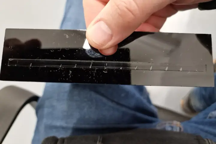 A hand holds a black acrylic strip with a precisely cut slot, demonstrating how to laser cut acrylic at home.