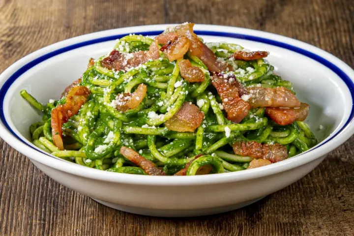 Un piatto invitante di pasta con spinaci, condita con croccante pancetta e parmigiano grattugiato, servita in una ciotola bianca con bordo blu.