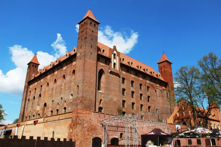 Potężny zamek w Gniewie, ceglana twierdza z wieżami i czerwonymi dachami, pod błękitnym niebem. Ciekawostki o jego historii czekają na odkrycie.