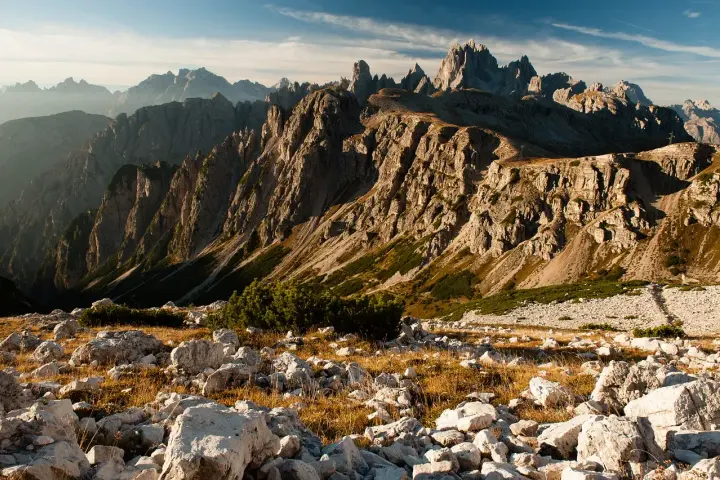 Skaliste szczyty Dolomitów o wschodzie słońca, z kamienistym zboczem i suchą trawą na pierwszym planie.
