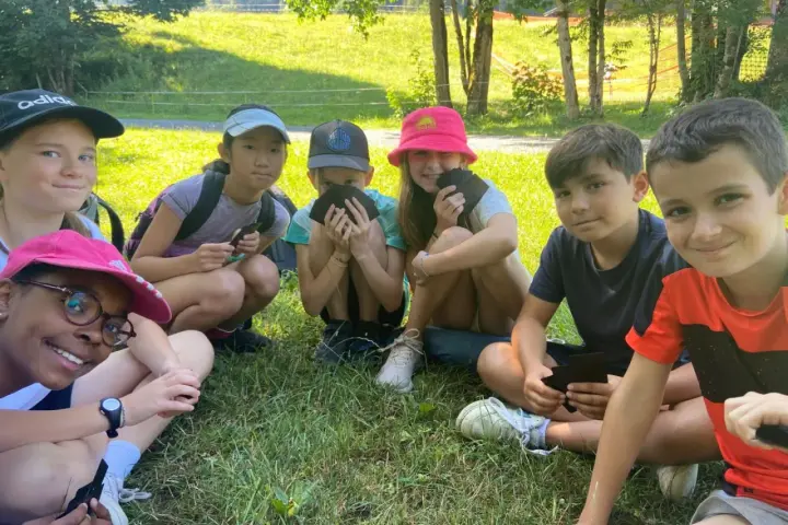 Groupe d'enfants souriants assis dans l'herbe, certains tenant des cartes.