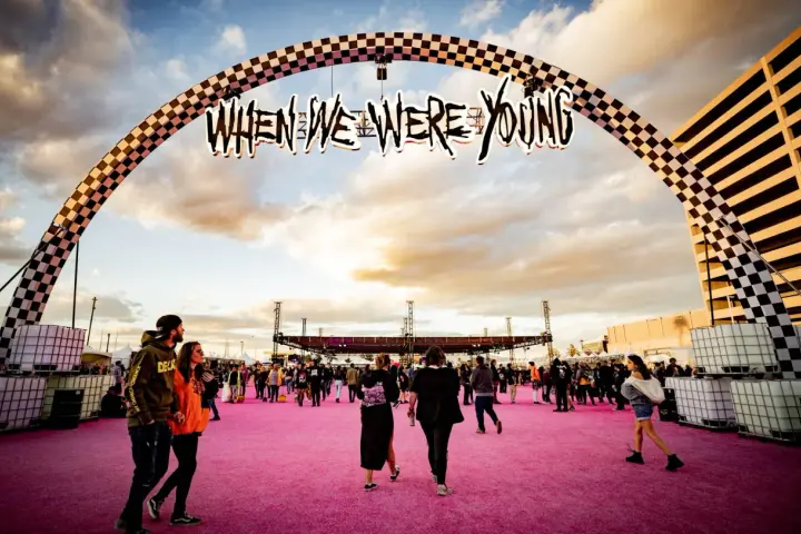 Gente camina bajo un arco con el letrero "When We Were Young Festival" sobre una alfombra rosa.