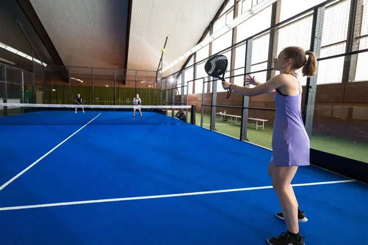 En kvinna i lila klänning spelar padel. Hon är redo att slå bollen på den blå banan.