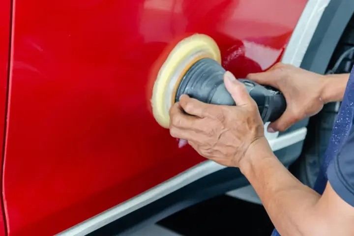 Ręce polerują czerwony lakier auta maszyną polerską. To kluczowy etap, jak woskować auto, by uzyskać lustrzany połysk i ochronę.