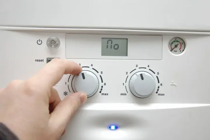 Dłoń reguluje pokrętłem pieca, przygotowując dom na nadchodzący sezon grzewczy. Na wyświetlaczu widnieje "110".